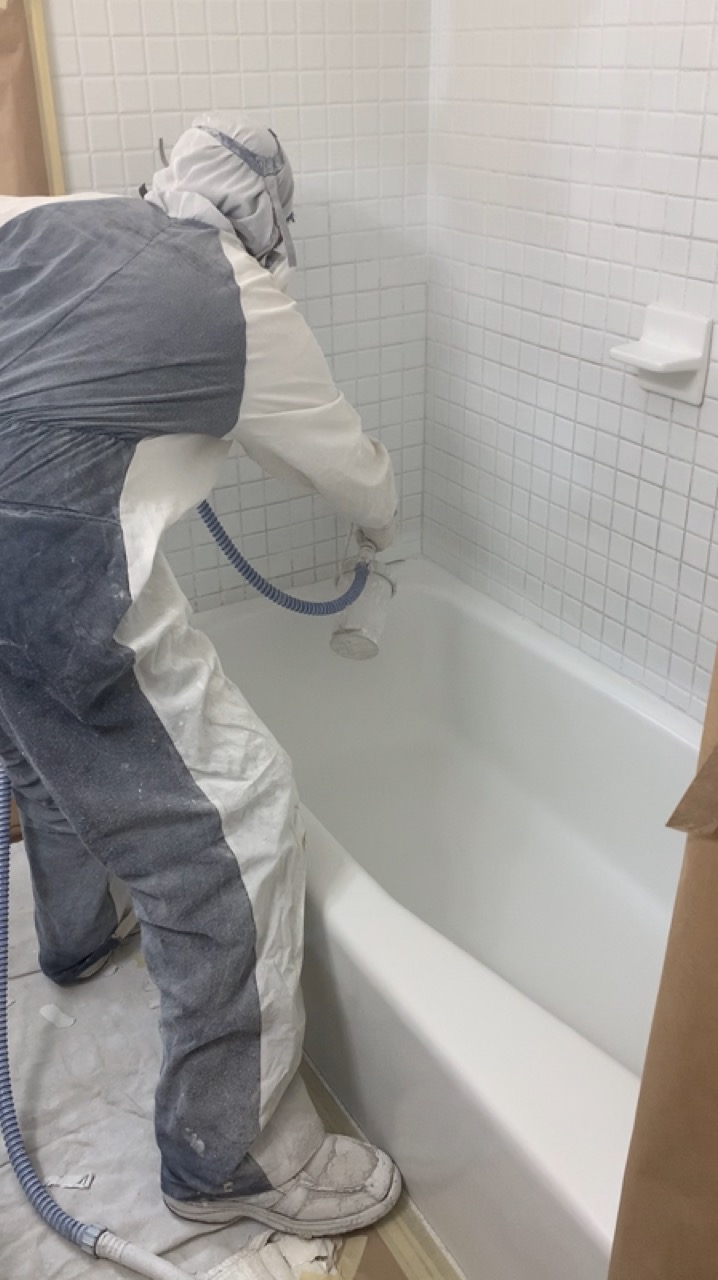Technician refinishing a bathtub with a spray gun